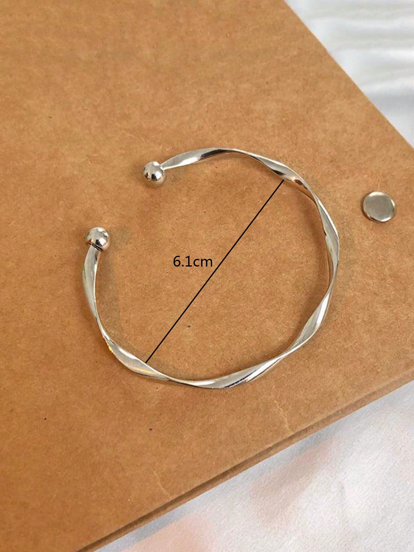 Silver twisted bangle bracelet with a ball accent on one end. Elegant, minimalist design displayed on a gray fabric background