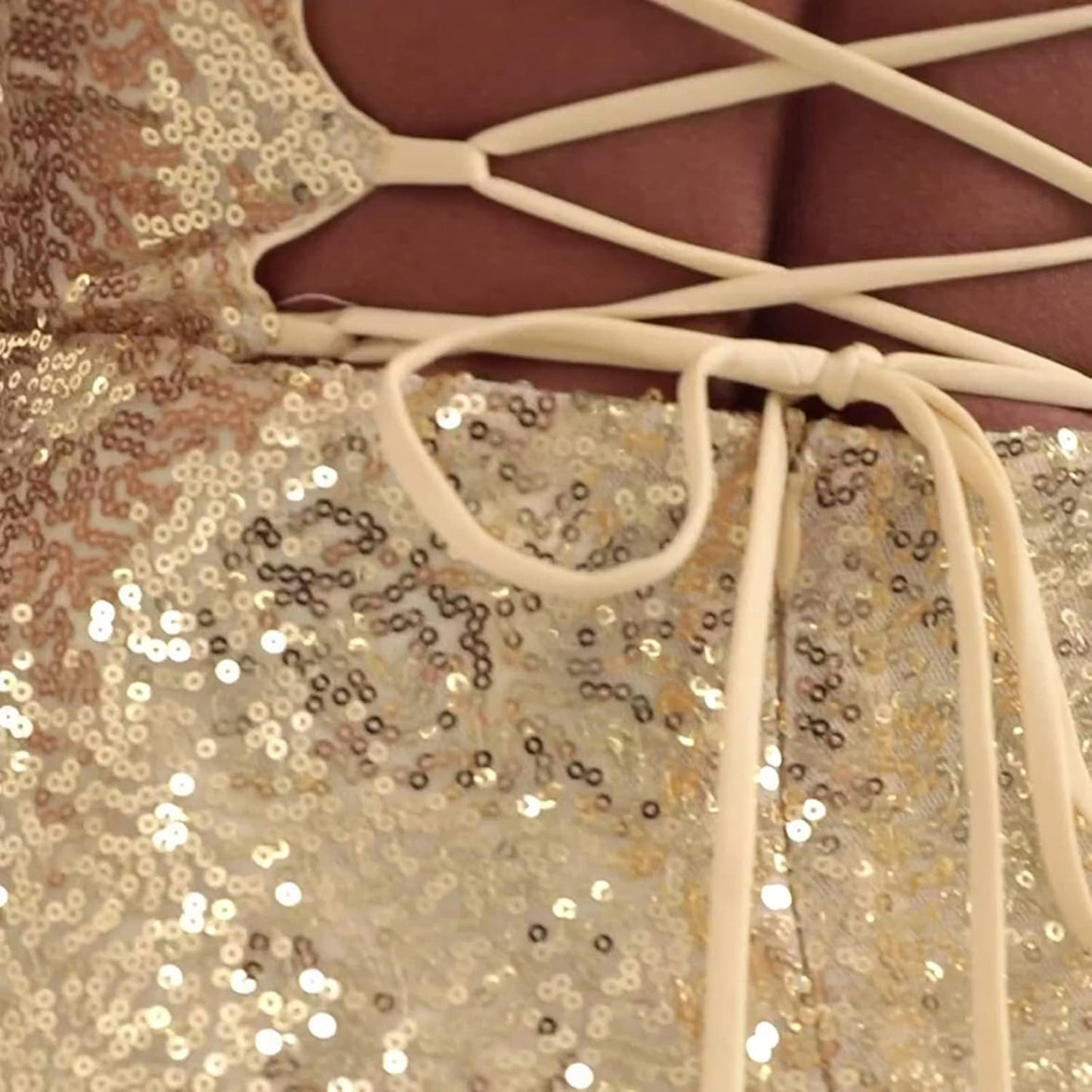Close-up view of a gold sequined dress with thin shoulder straps and crisscross lace-up back detail.