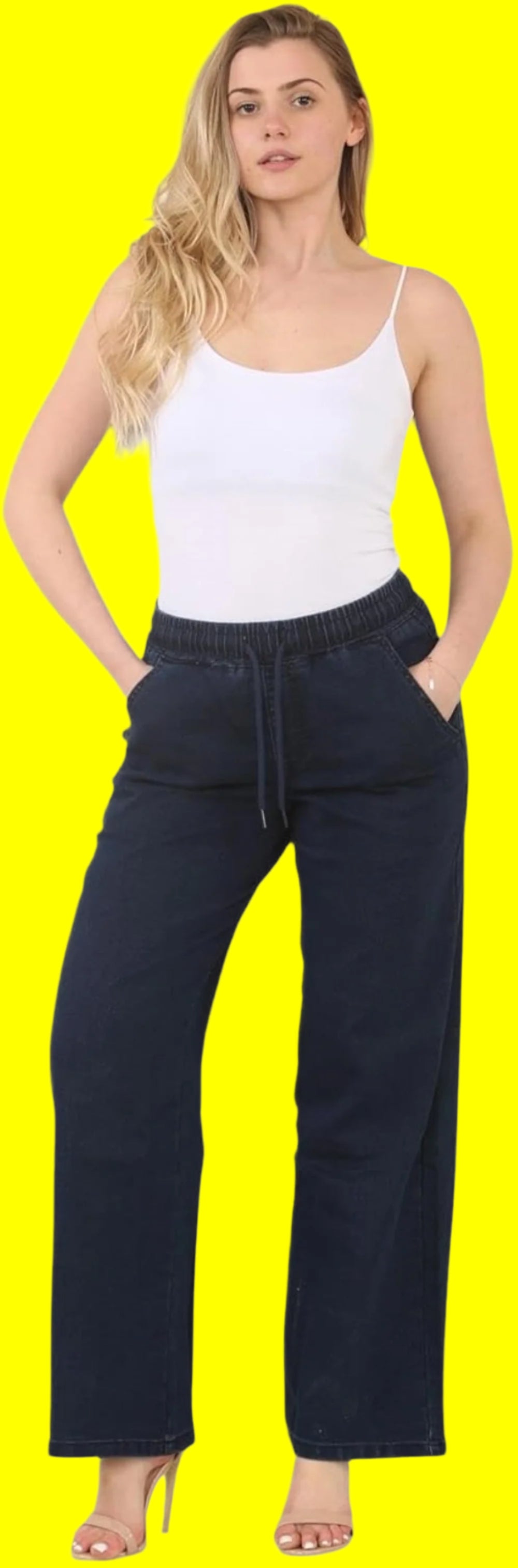 Woman modeling a white tank top paired with navy blue wide-leg pants, standing against a bright yellow background with hands in pockets.