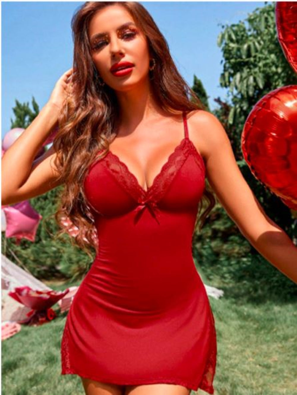 Red lace lingerie set with deep V-neckline and side slit. Features a fitted bodice and flowing skirt with lace hem. Model stands outdoors with decorative balloons in the background.