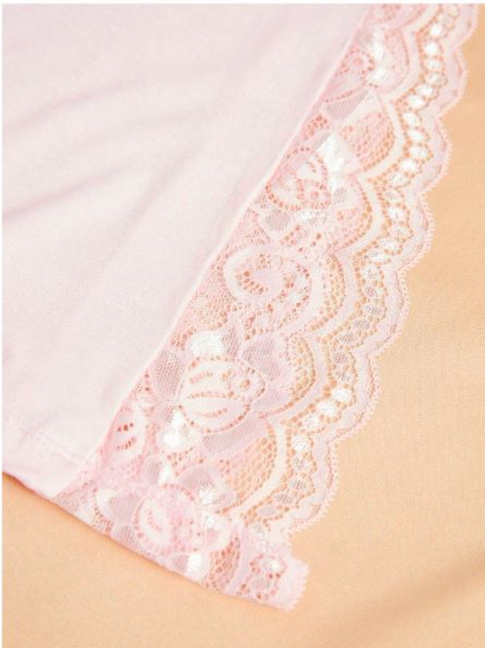 Close-up of pink lace trim with floral pattern and scalloped edges. The lace is delicate with intricate detailing, laid against a soft pink fabric background