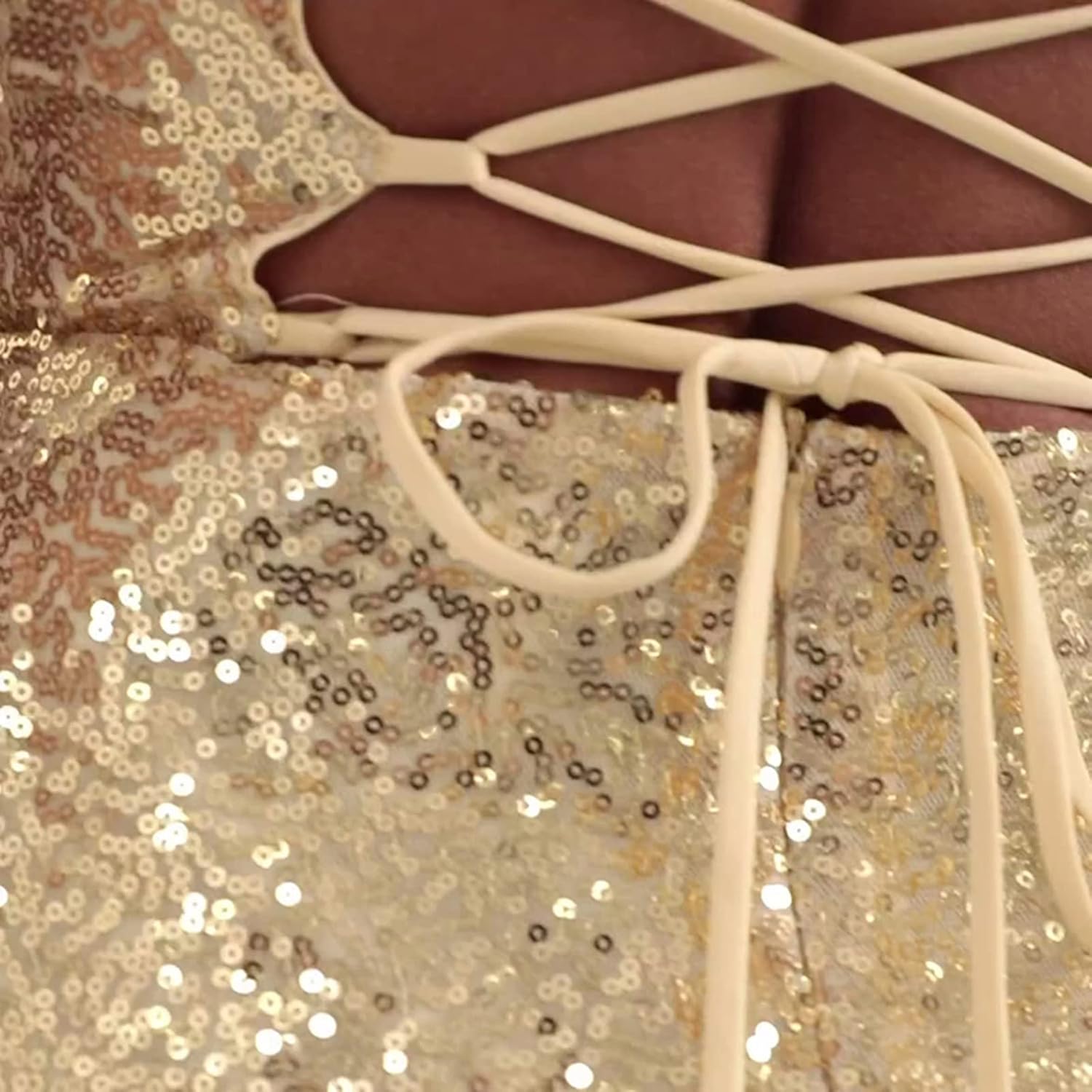 Close-up view of a gold sequined dress with thin shoulder straps and crisscross lace-up back detail.