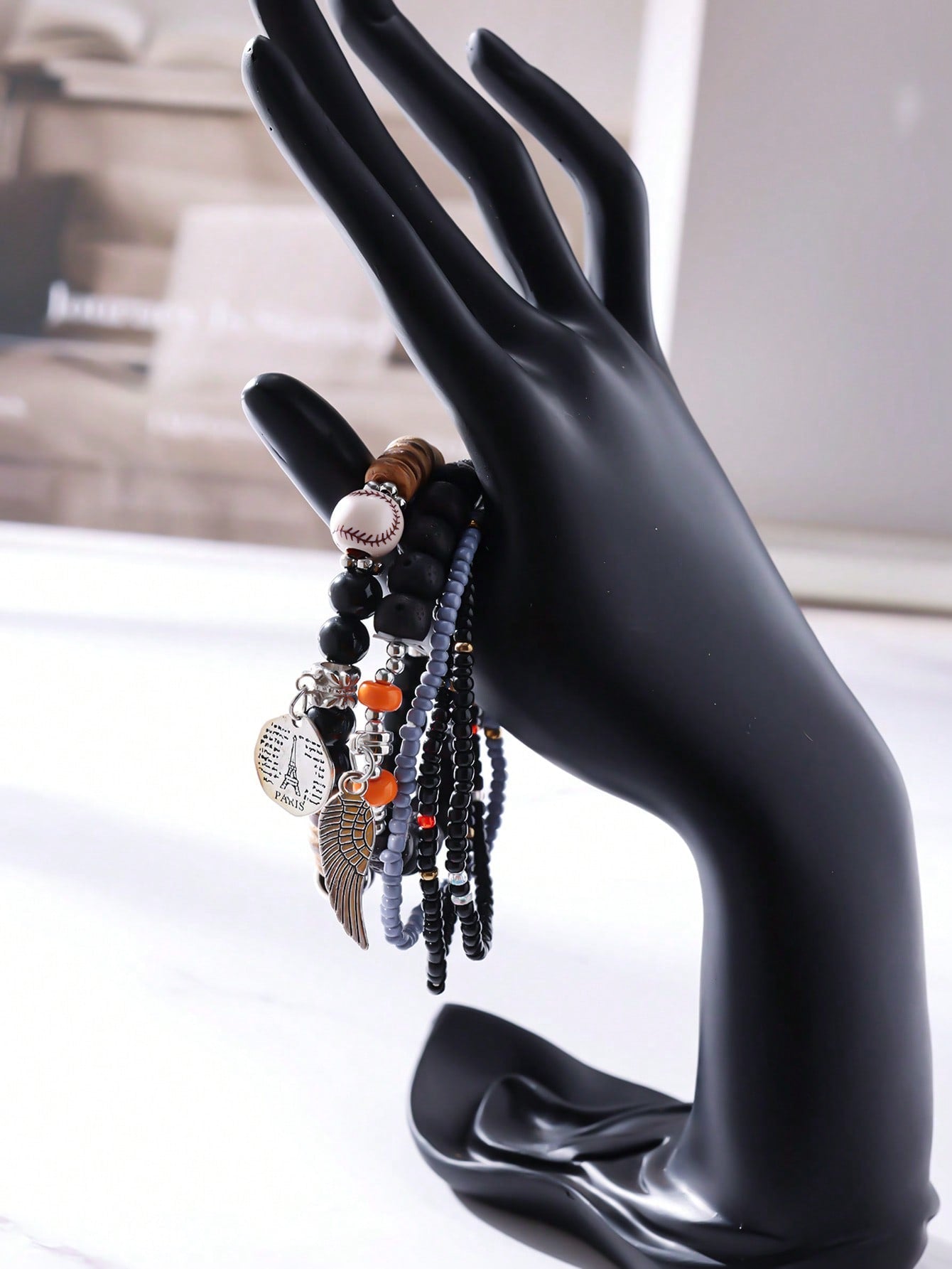Stack of multicolored beaded bracelets featuring blue, white, and wooden beads with gold accents. Includes a silver wing charm and a round pendant engraved with 'PARIS'. Layered design for a vibrant, travel-inspired look.