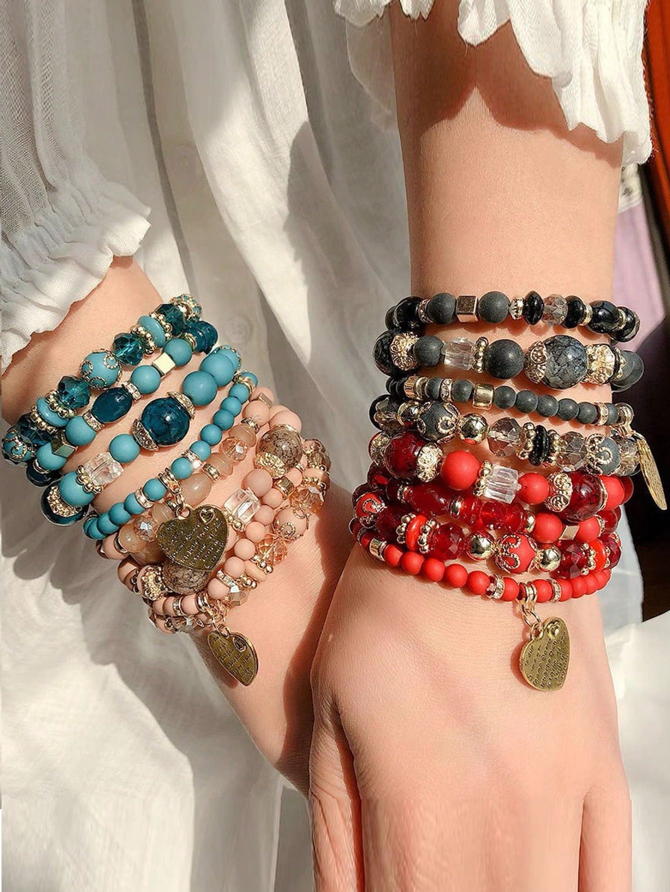Stack of multicolored beaded bracelets in blue, pink, red, and gray tones with gold accents and charm details. Layered design with varying bead sizes and textures for a vibrant, bohemian look.