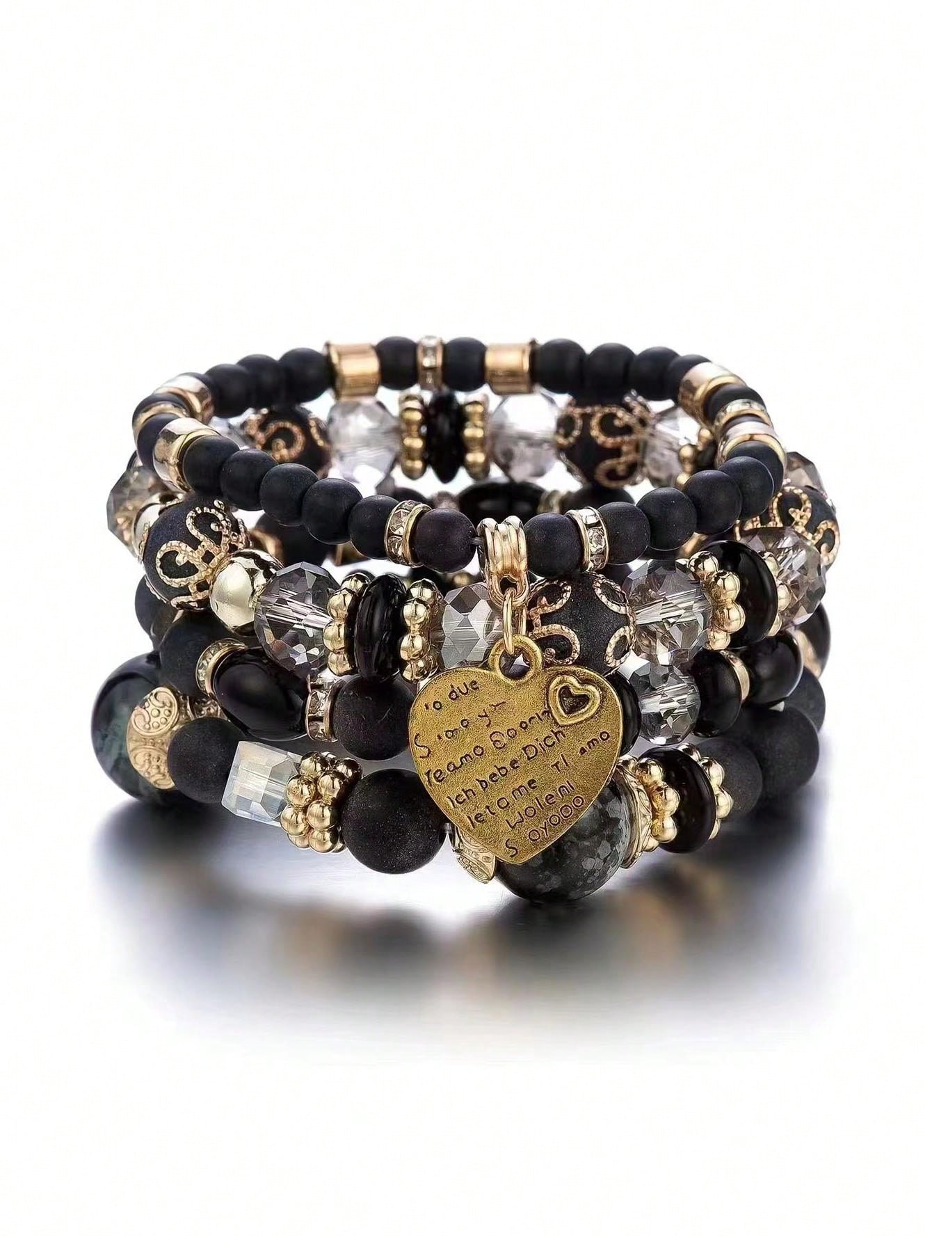 Stack of black beaded bracelets with gold accents and clear crystal beads. Features a gold heart-shaped charm with engraved text. Layered design for a versatile, elegant look