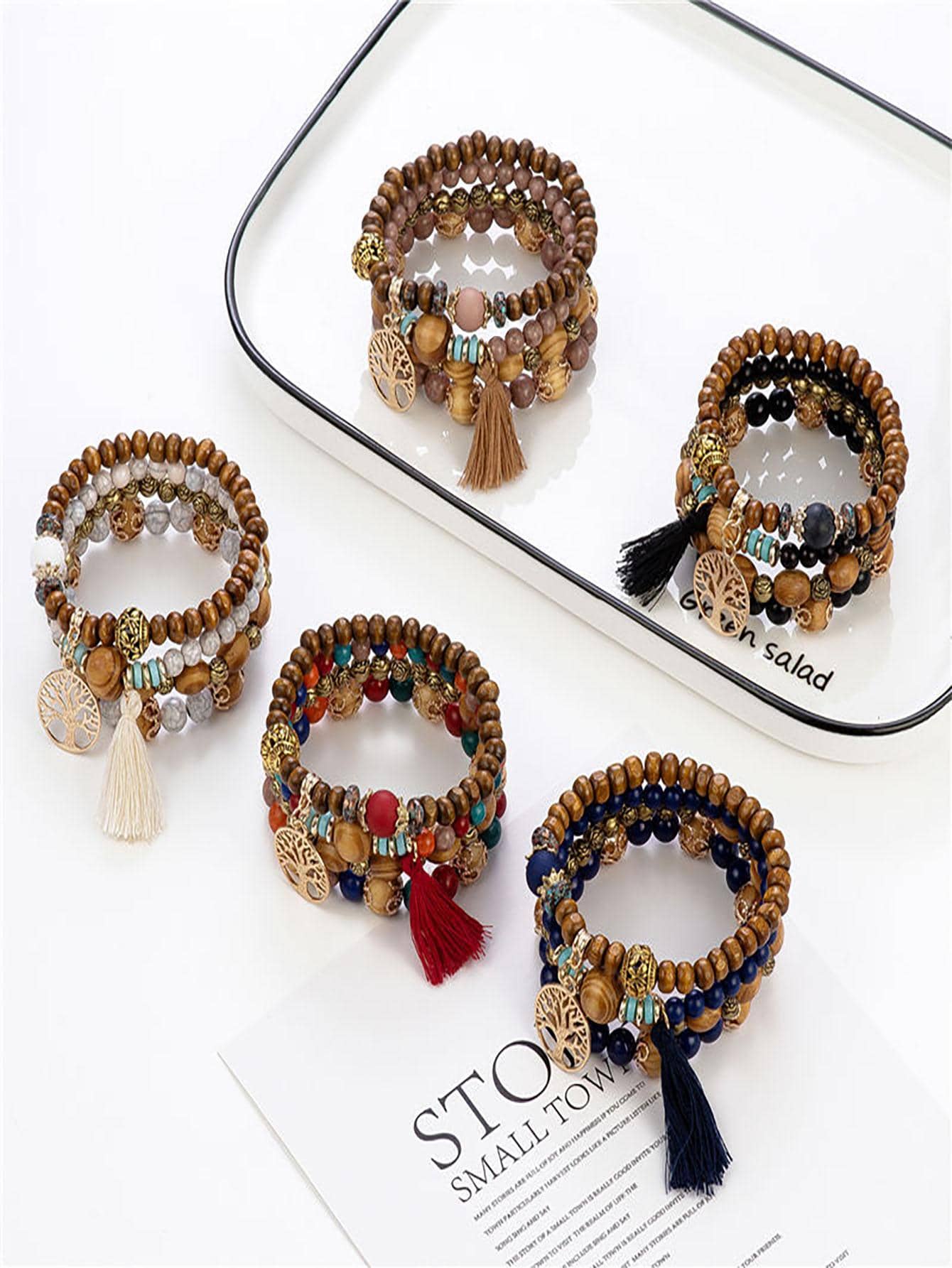 Set of four beaded bracelets with wooden beads, gold accents, and tassels. Includes neutral, rainbow, navy blue, and dark brown variations with black beads. Bohemian style displayed on a white surface with a mirrored tray.