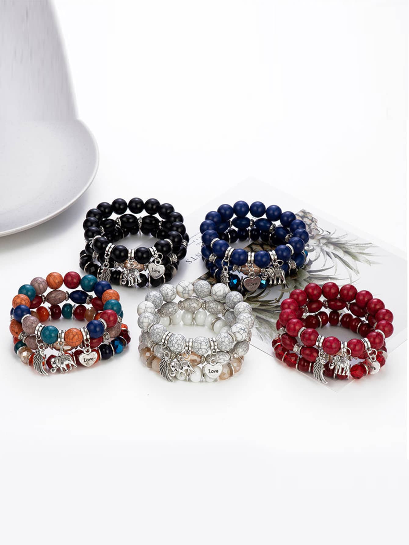 Set of five beaded bracelets in black, blue, multicolor, white, and red with silver charms. Features elephant and heart pendants with 'Love' text. Displayed on a white surface.