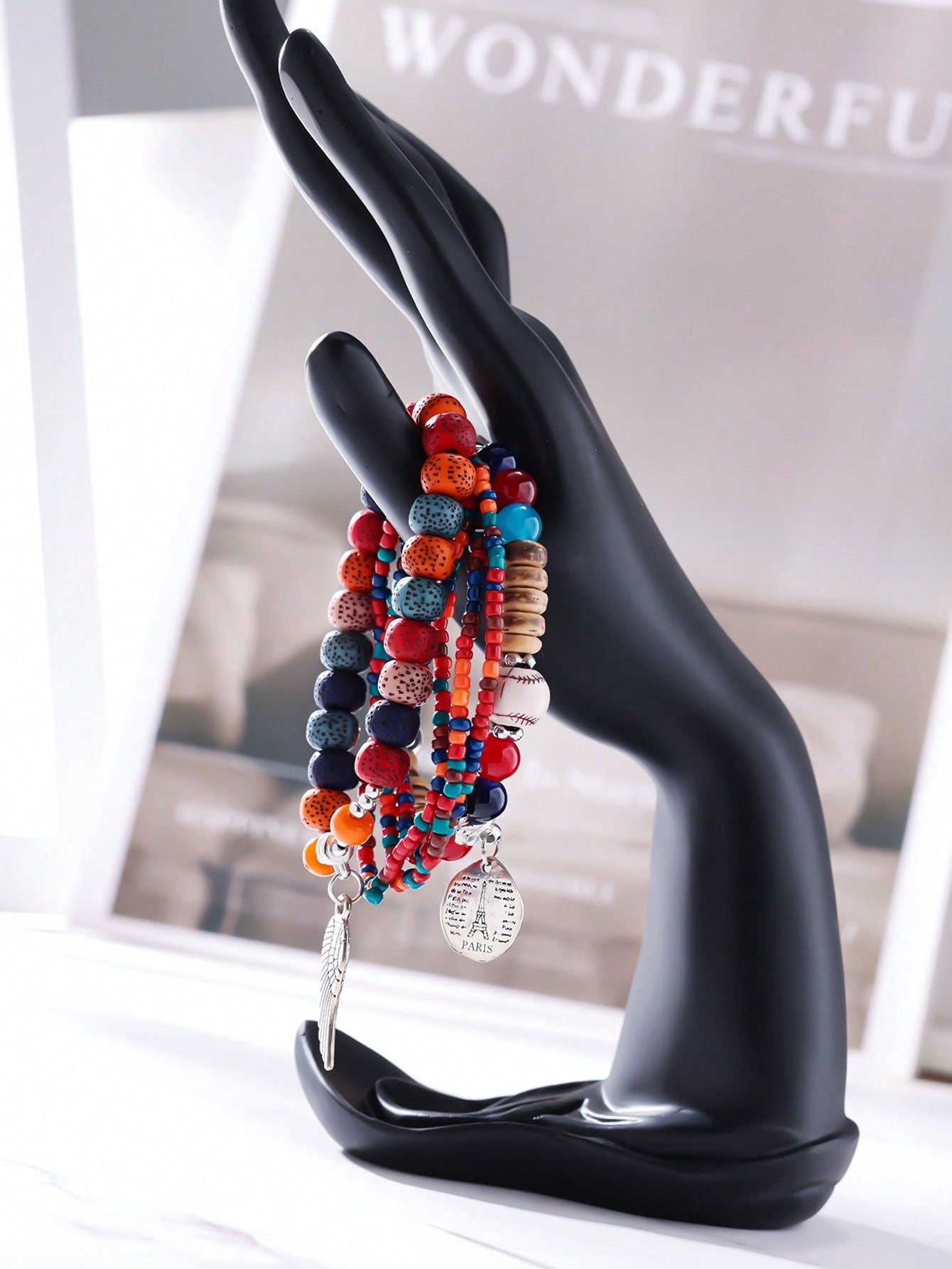 Stacked multicolor bracelet set with red, blue, and transparent beads. Includes wood accents, patterned beads, and clear bands. Features a metallic wing pendant and round Eiffel Tower charm engraved with 'PARIS' and script text. Versatile design for layering or gifting.