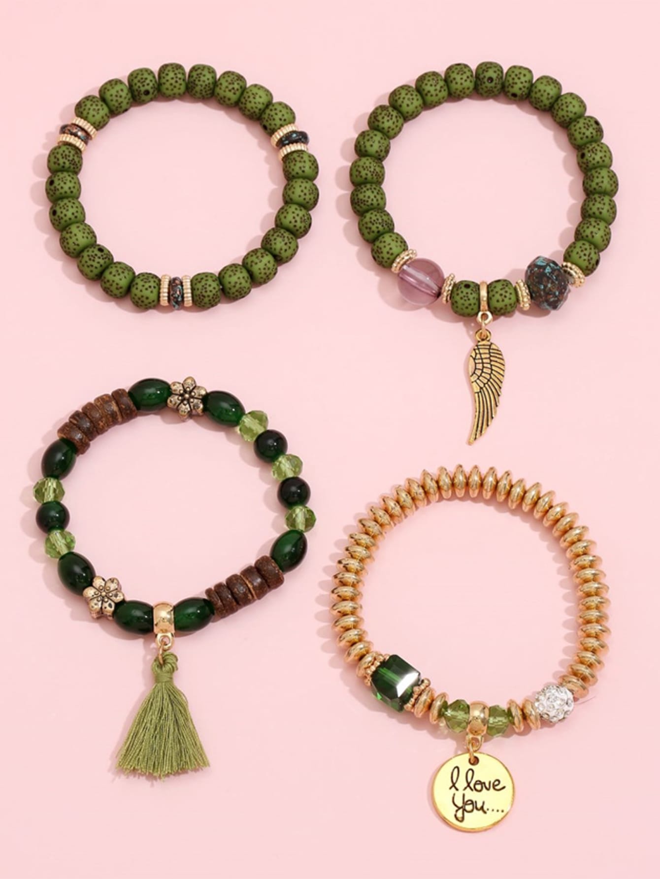 Set of four green beaded bracelets with gold accents and charm details. Includes a wing charm, heart pendant with 'I love you' text, tassel, and mix of beads. Earthy design displayed on a pink background.