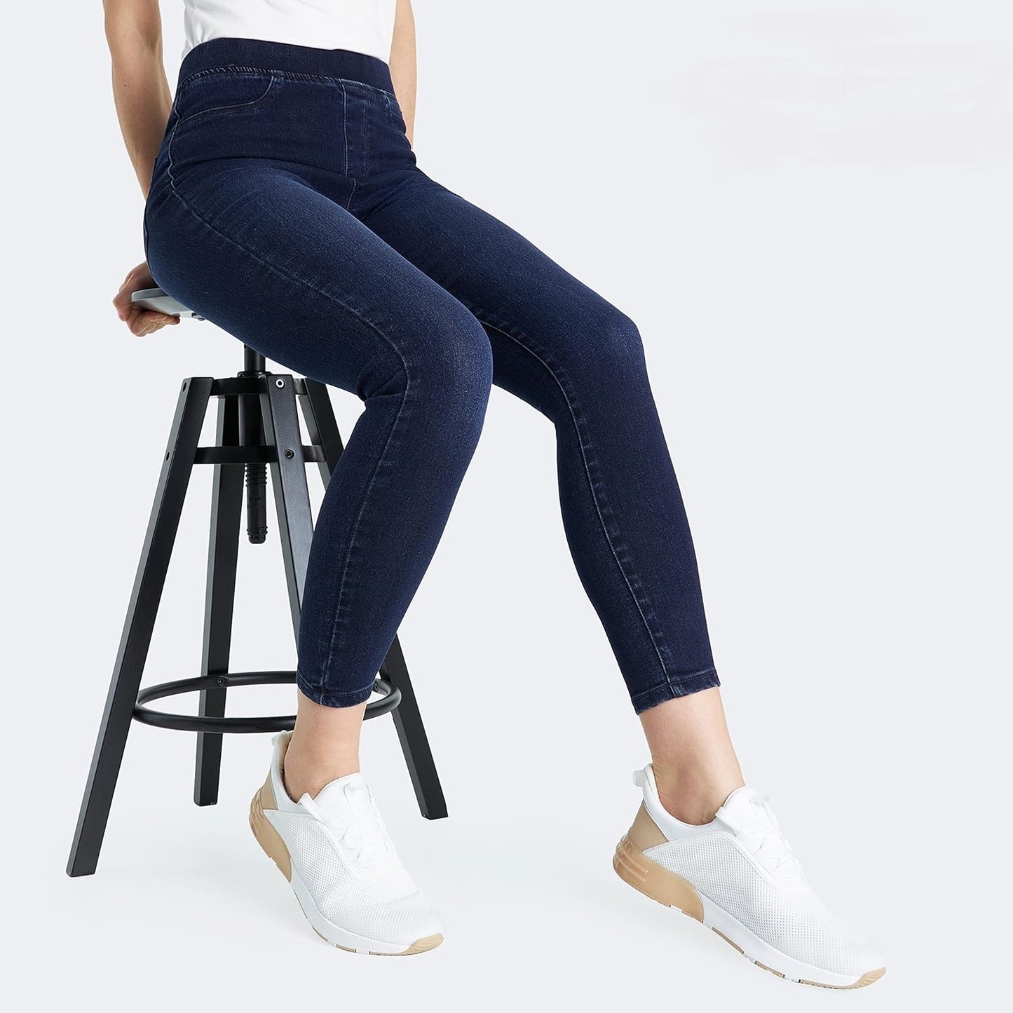 Woman wearing Indigo-Blue skinny jeans with a high waistband and white sneakers while sitting on a stool.