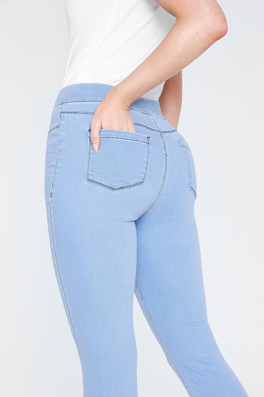 Woman wearing light blue skinny jeans with high waistband and back pockets, paired with a white short-sleeved shirt and white sneakers.