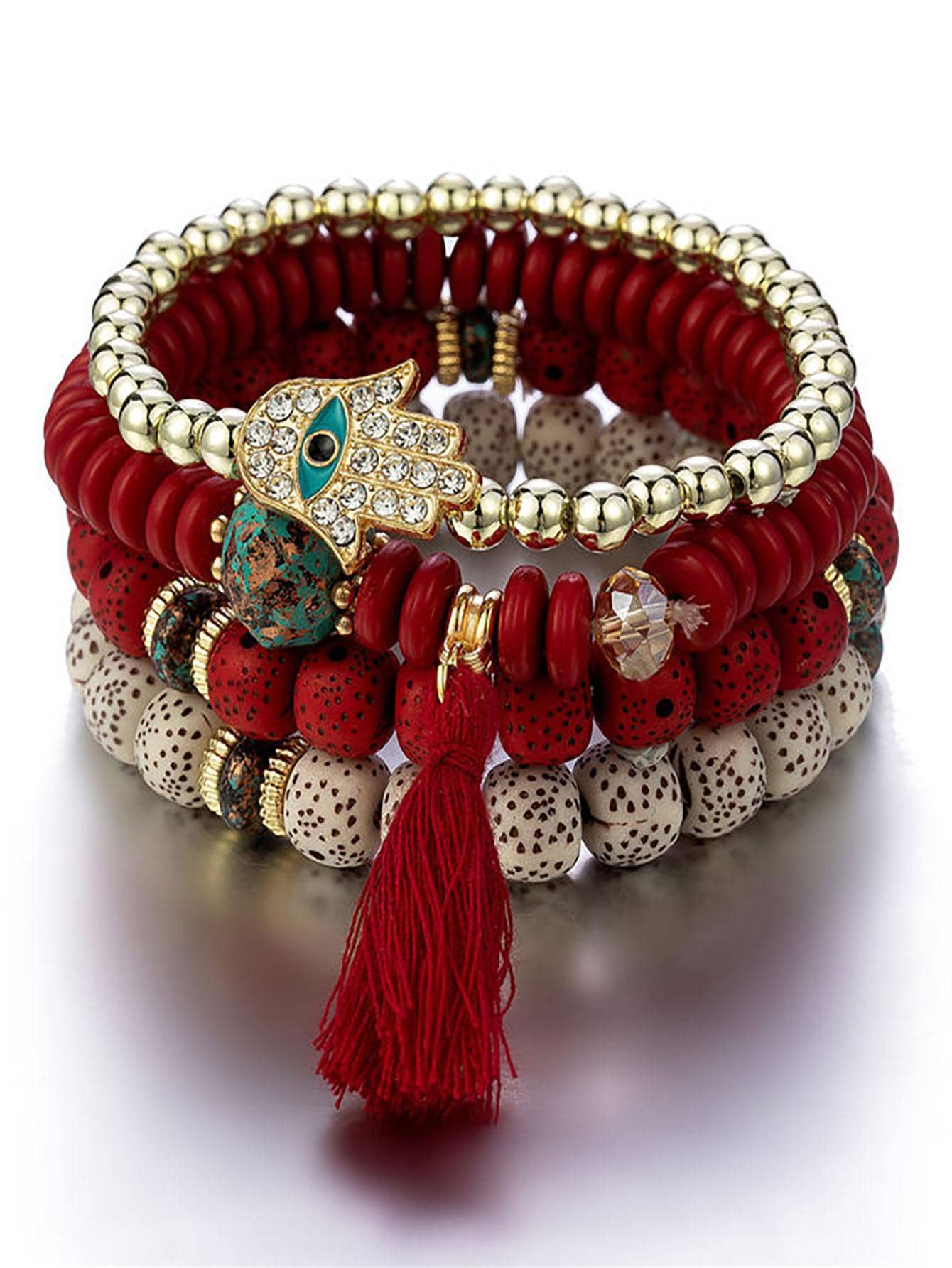 Stack of red beaded bracelets with gold accents featuring a gold Hamsa hand charm and red tassel. Bohemian style with varying bead textures and sizes.