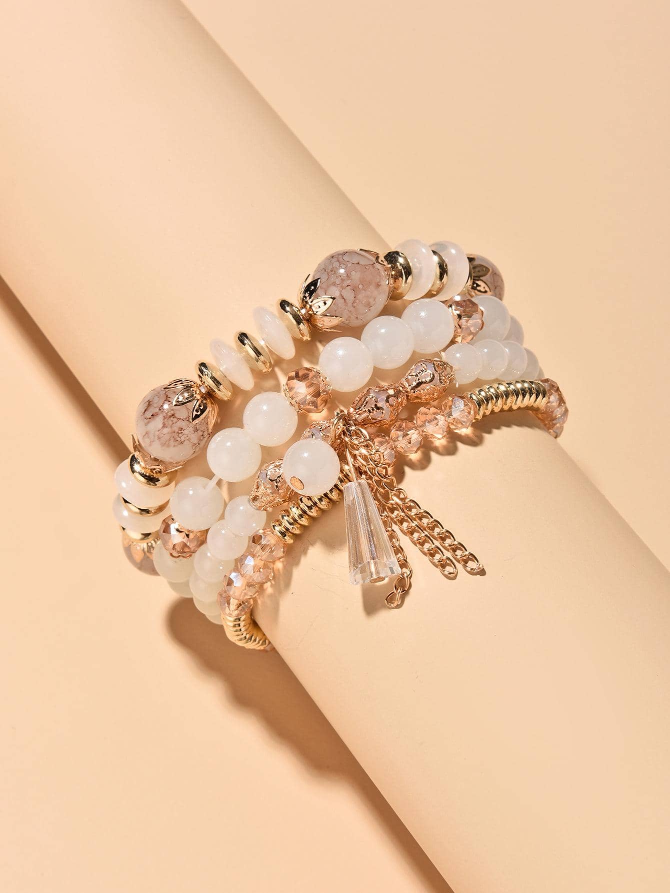 Stack of white beaded bracelets with gold accents and charm details. Layered design with varying bead sizes and gold chain elements for an elegant, bohemian style.